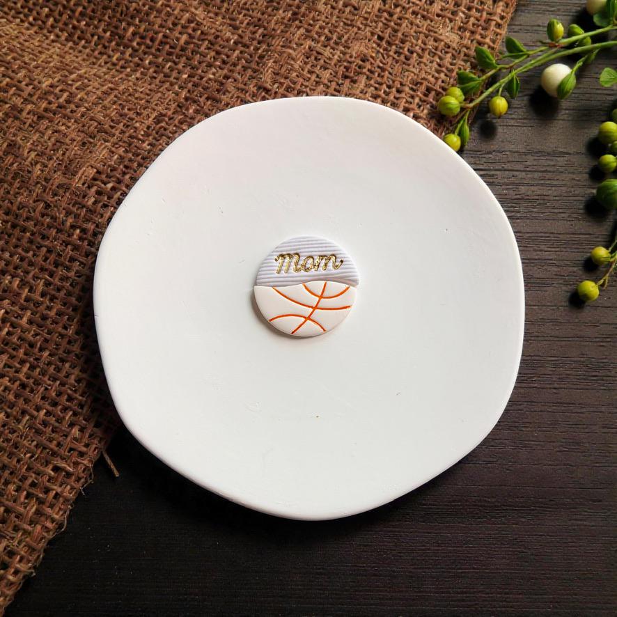 Finished basketball mom polymer clay earring displayed on white ceramic plate with rustic wood background