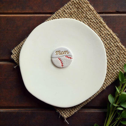 Finished baseball mom polymer clay earring displayed on white ceramic plate with rustic wood background