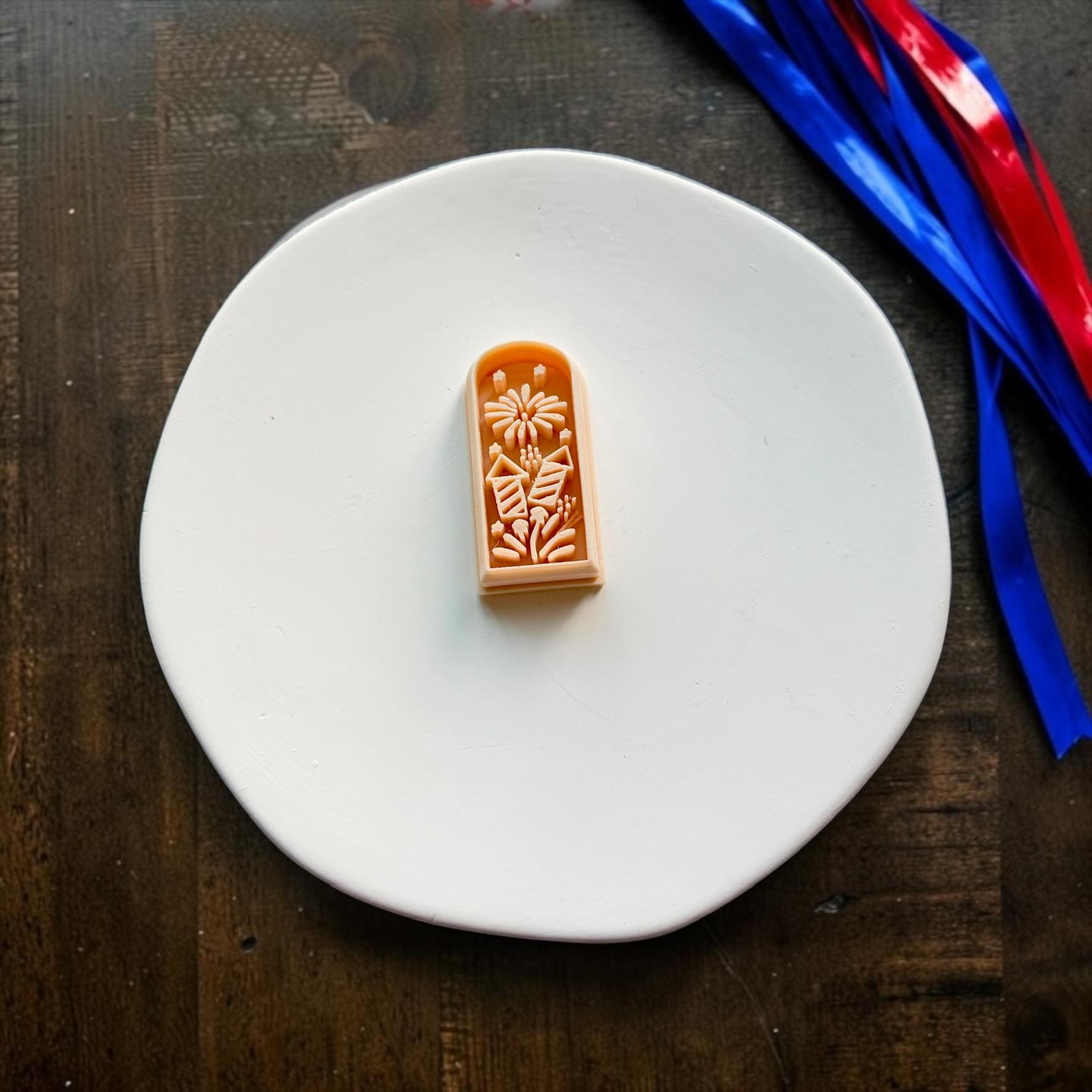 Fireworks themed polymer clay cutter displayed on a white ceramic plate with patriotic ribbon accents