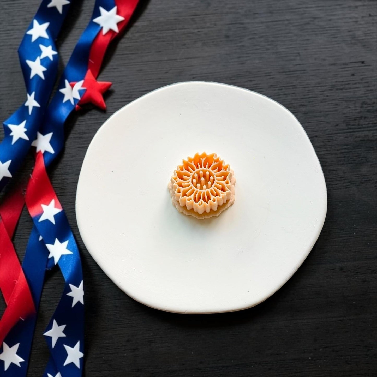 Patriotic sunflower polymer clay cutter displayed on a white ceramic plate with red white and blue ribbon accents