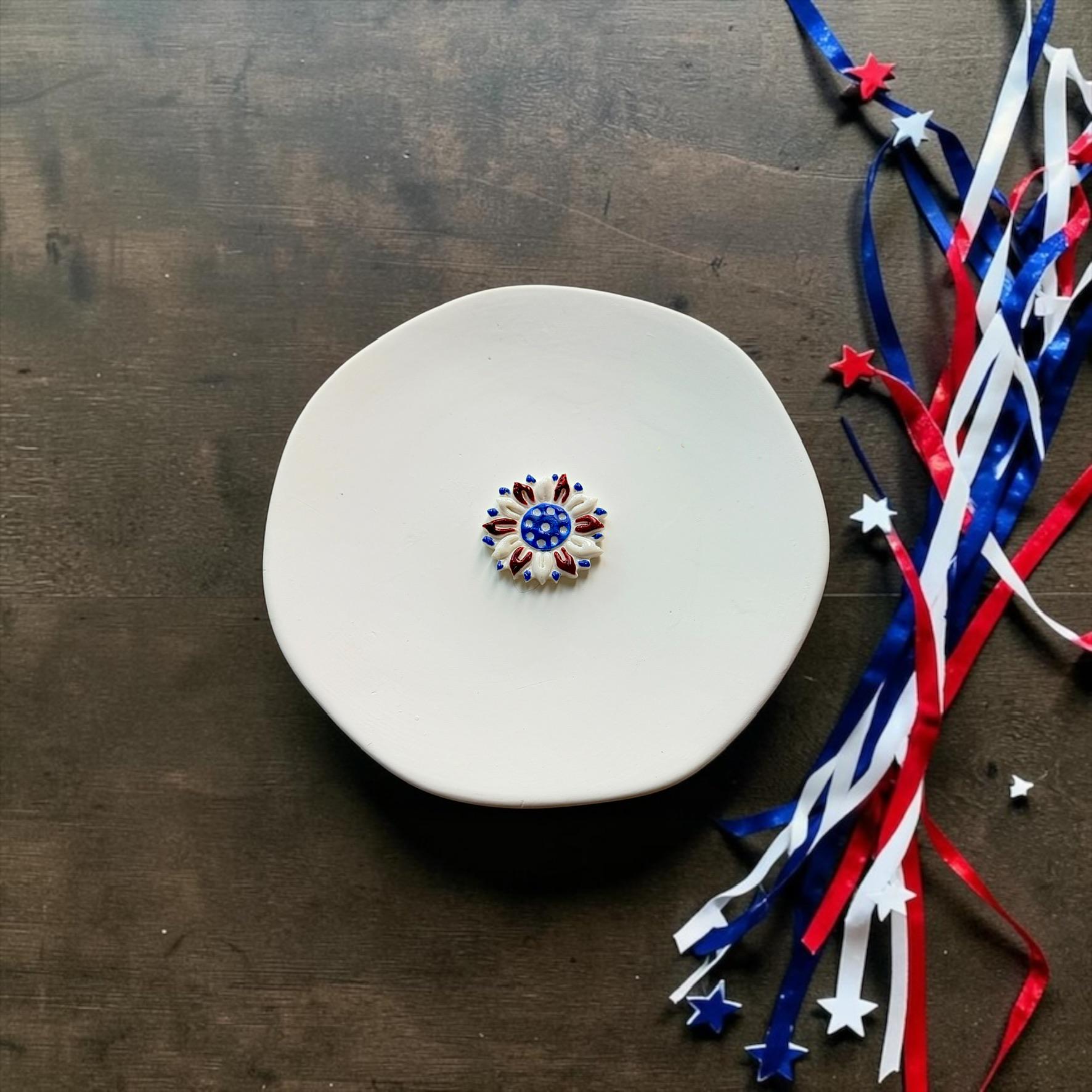 Finished patriotic sunflower clay piece in red white and blue displayed on a white ceramic plate