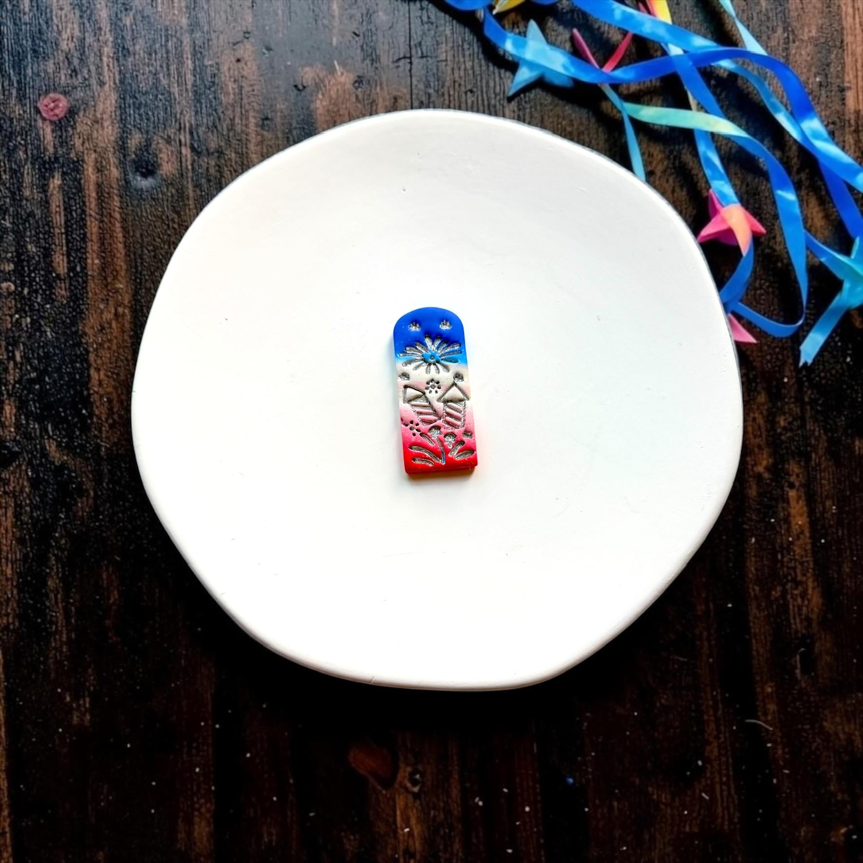 Finished red white and blue clay piece featuring fireworks and patriotic details on a white ceramic plate
