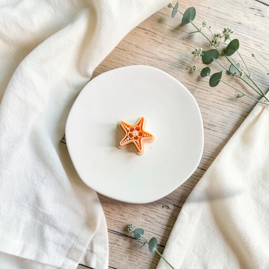 Starfish polymer clay cutter displayed on a white ceramic plate with neutral fabric and greenery.