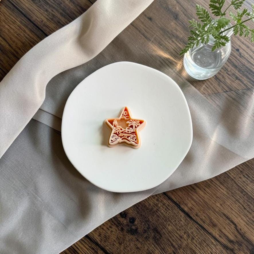 Beach scene star polymer clay cutter displayed on a white ceramic plate with neutral fabric and greenery.