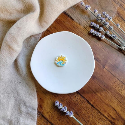 Finished sunrise and wave polymer clay earring displayed on a white ceramic plate with dried lavender.