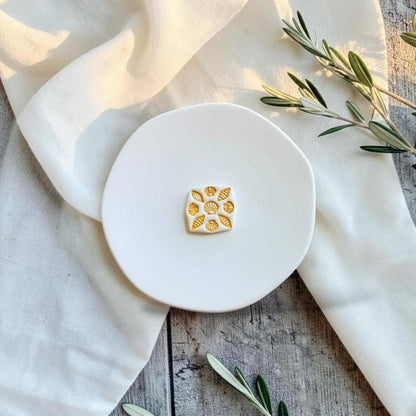 Finished white polymer clay seashell tile earring with gold detailing displayed on a white ceramic plate.