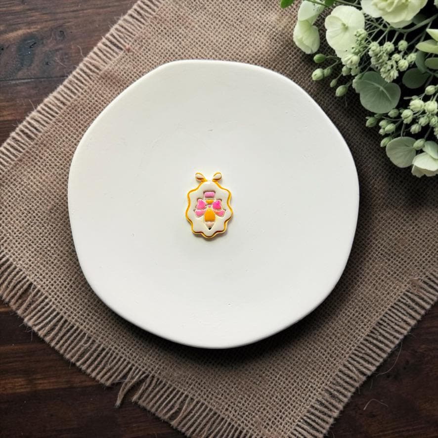 Finished pencil with bow framed polymer clay earring displayed on a white ceramic dish.