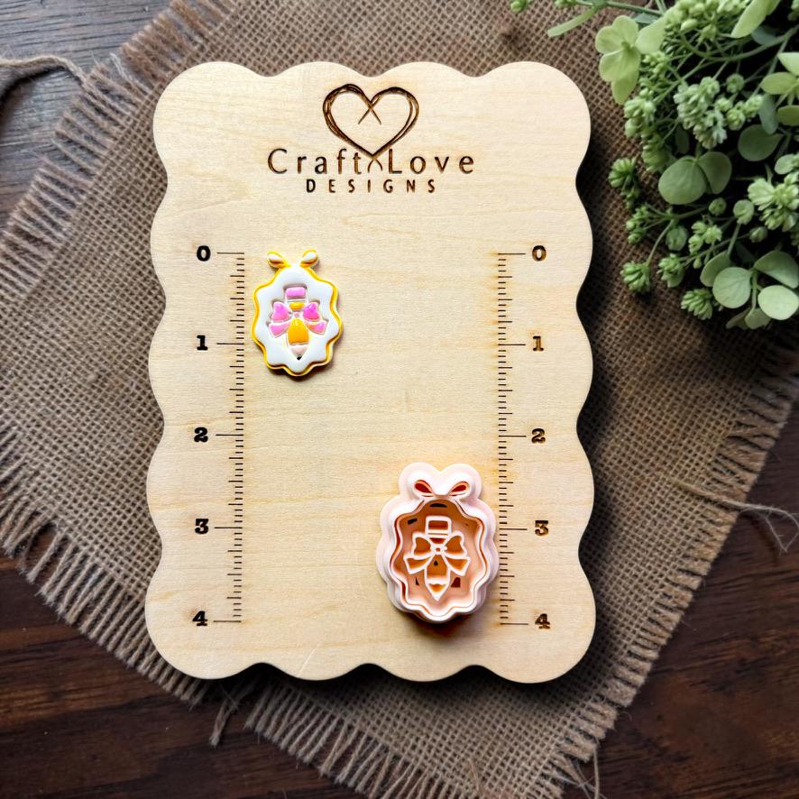 Finished pencil with bow framed earring and cutter displayed together on the Craft Love Designs measurement board.
