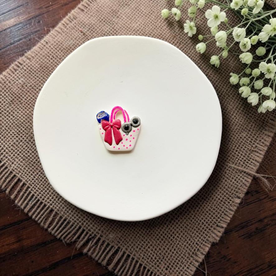 Finished summer handbag polymer clay earring displayed on a white ceramic dish.