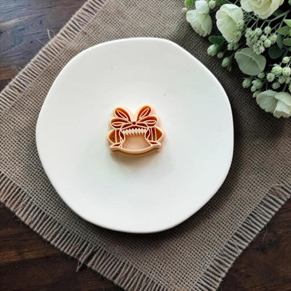 Peach polymer clay cutter featuring a football topped with a large coquette bow, displayed on a white plate.