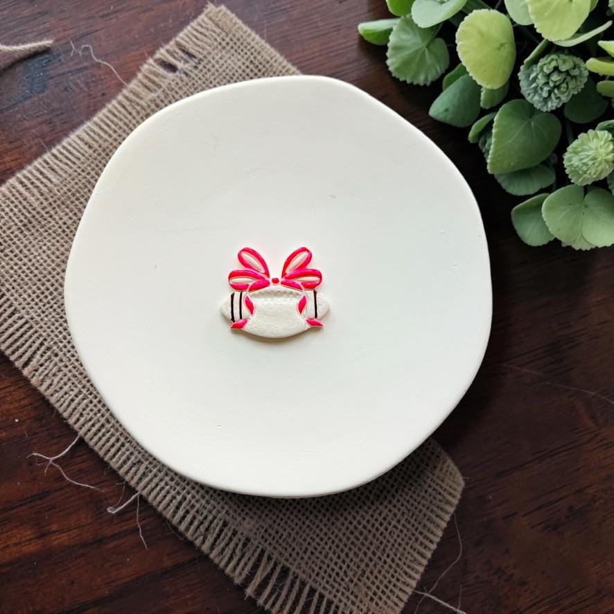 Finished white football clay design topped with a large bright pink coquette bow, displayed on a white plate.