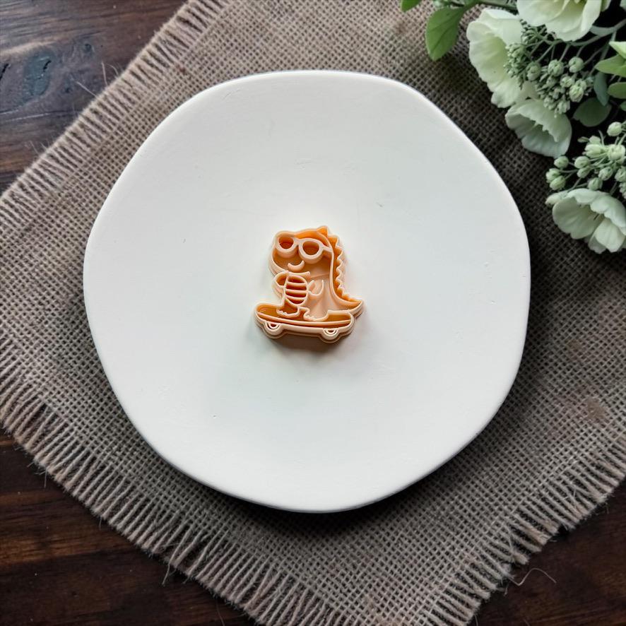 Peach polymer clay cutter featuring a gator wearing sunglasses and riding a skateboard, displayed on a white plate.