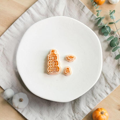 Stacked pumpkin polymer clay cutter with separate ghost and bat detail pieces displayed on a white plate with autumn decor.
