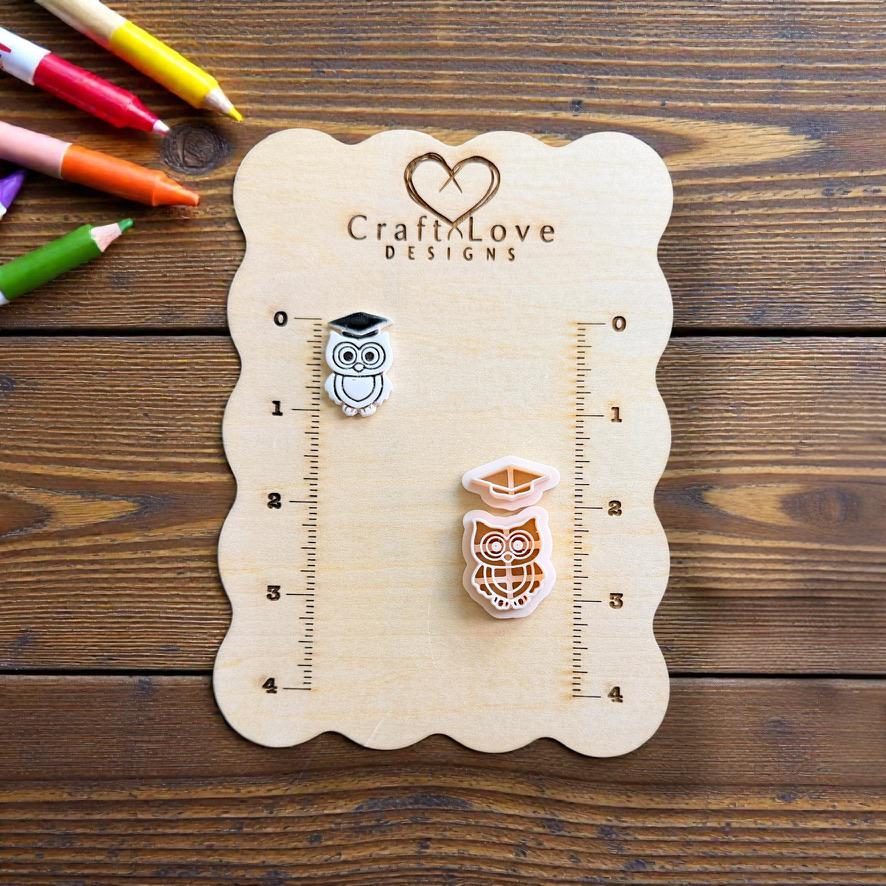 Finished graduation owl and matching two-piece polymer clay cutter displayed on a measurement board with school supplies in the background.