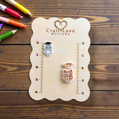 Finished graduation owl and matching two-piece polymer clay cutter displayed on a measurement board with school supplies in the background.