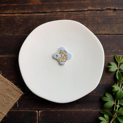 Finished light blue clay piece featuring a detailed gold cluster of whimsical mushrooms and botanical elements displayed on a white plate.