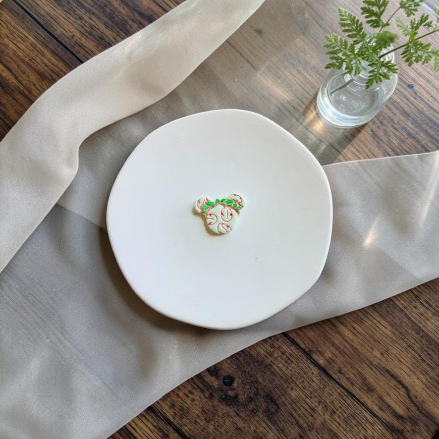Finished white Aloha Mouse polymer clay piece decorated with pink tropical floral details and green foliage on a white display plate.