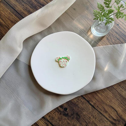 Finished white Aloha Mouse polymer clay piece decorated with pink tropical floral details and green foliage on a white display plate.