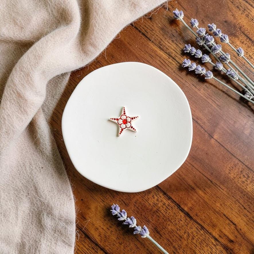 Finished white and red starfish clay earring displayed on a white ceramic plate with lavender accents.