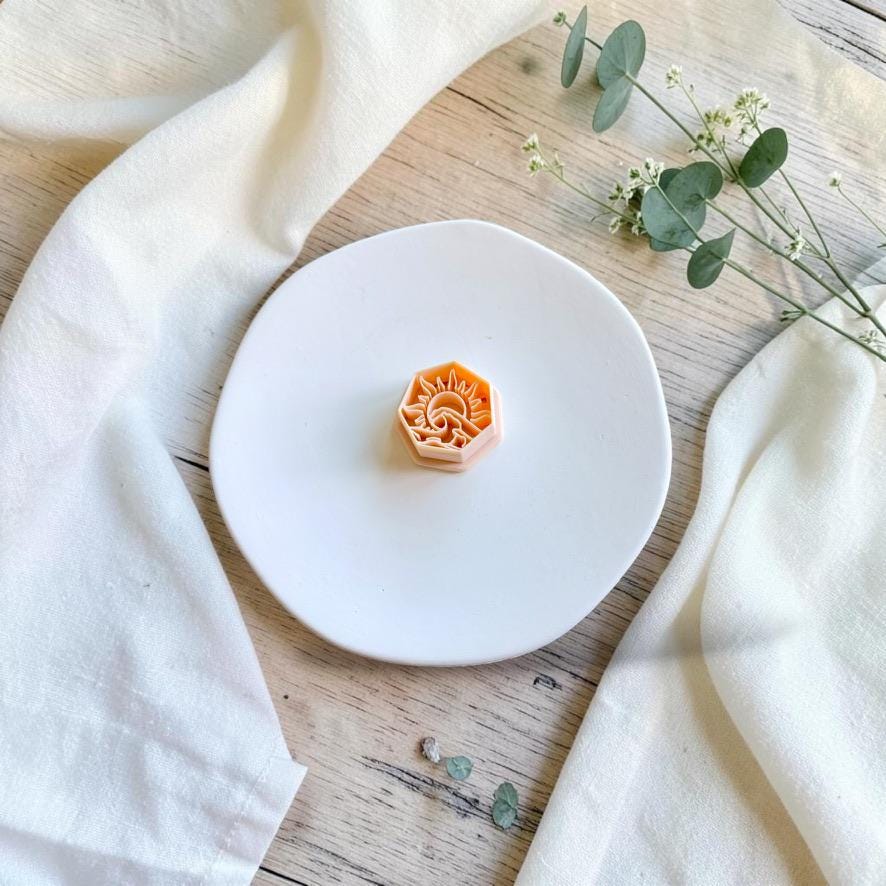 Hexagon polymer clay cutter with an intricate sunrise and ocean wave design displayed on a white ceramic plate.