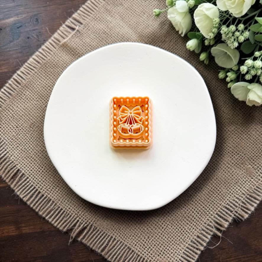 Rectangular football cherry and bow polymer clay cutter on a white ceramic dish.