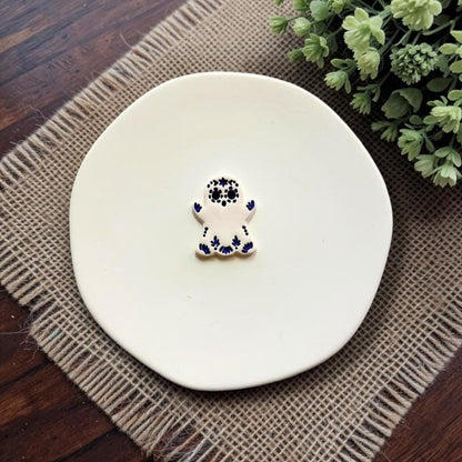 White sugar skull ghost embossed polymer clay sample on white ceramic dish.