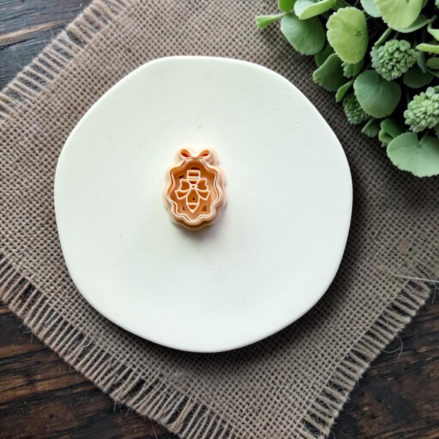 Pencil with bow framed polymer clay cutter displayed on a white ceramic dish.