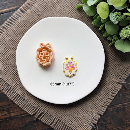 Pencil with bow framed cutter and finished sample displayed together on a white ceramic dish showing the 35mm (1.37") size.