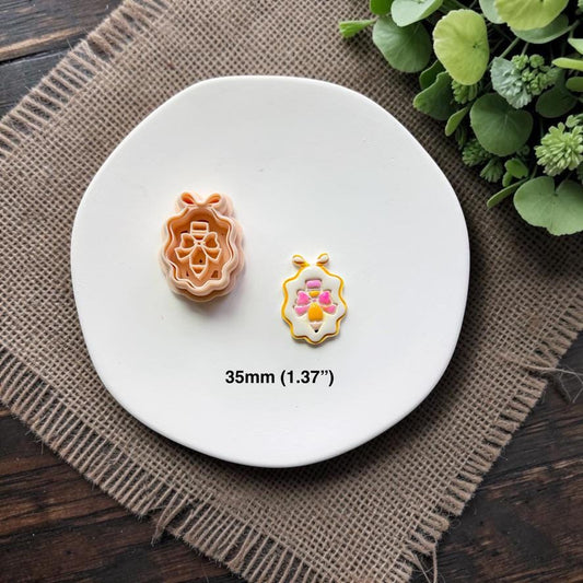 Pencil with bow framed cutter and finished sample displayed together on a white ceramic dish showing the 35mm (1.37") size.