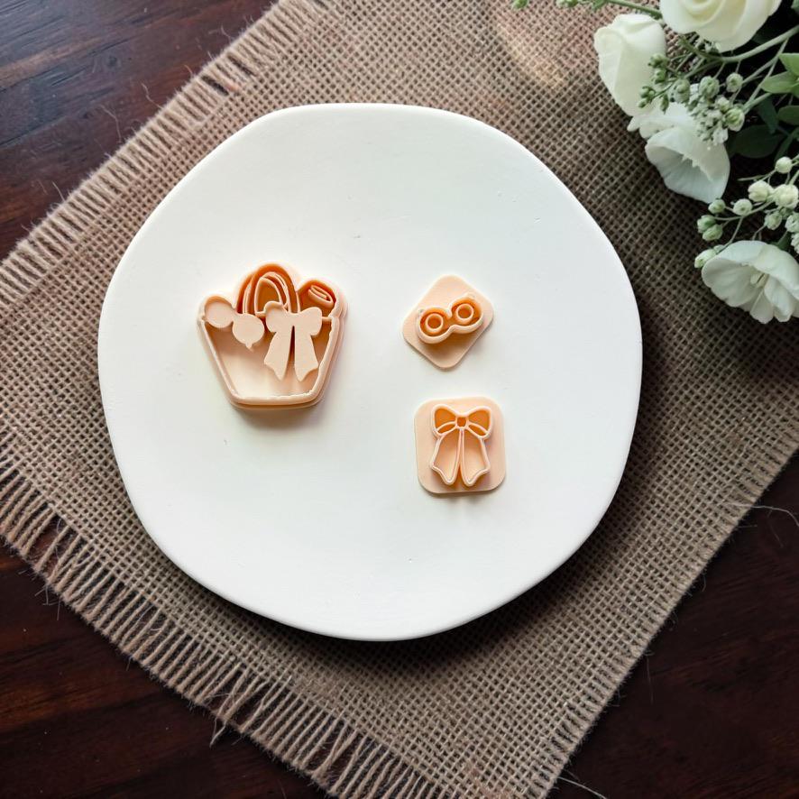 Summer handbag cutter with separate bow and sunglasses stamps displayed on a white ceramic dish.