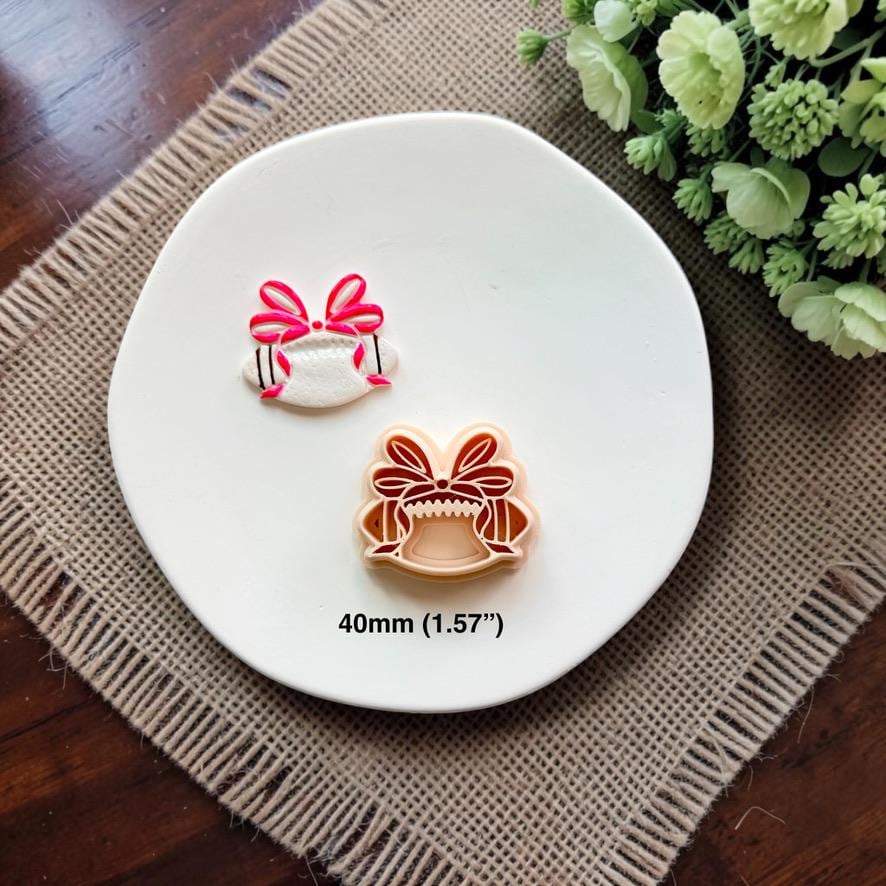 Finished white football clay piece with a bright pink coquette bow beside the matching 40mm polymer clay cutter.