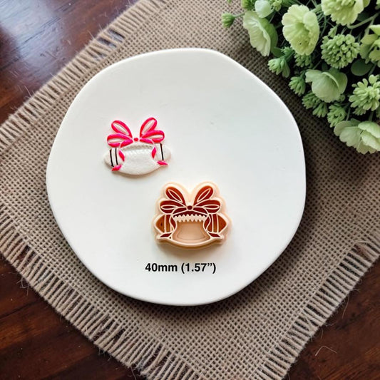 Finished white football clay piece with a bright pink coquette bow beside the matching 40mm polymer clay cutter.