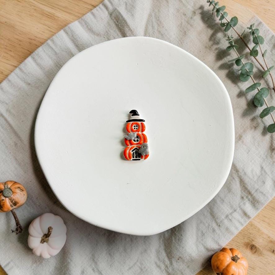 Finished orange stacked pumpkin design topped with a black witch hat and decorated with spooky details, displayed on a white plate with miniature pumpkins.