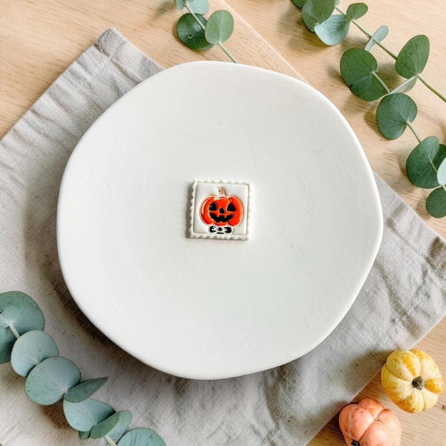 Finished orange and black jack-o-lantern pumpkin with bow inside a white decorative square frame displayed on a white plate.