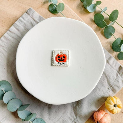 Finished orange and black jack-o-lantern pumpkin with bow inside a white decorative square frame displayed on a white plate.