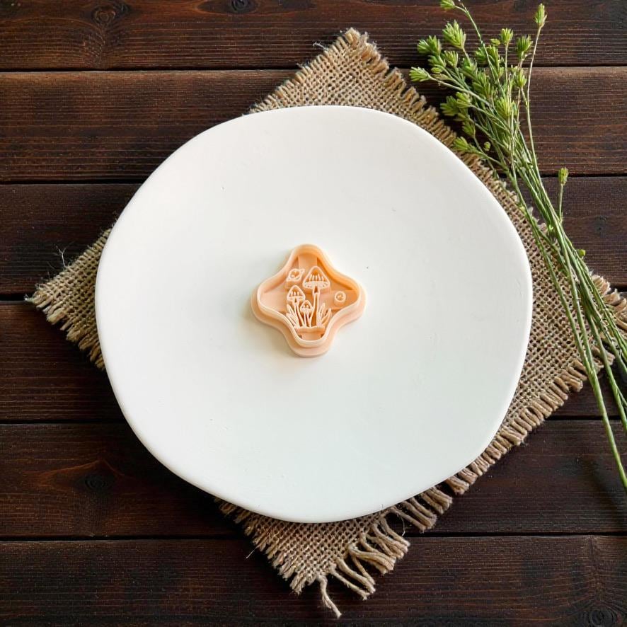 Mushroom polymer clay cutter featuring a detailed cluster of toadstools and woodland elements displayed on a white plate with rustic greenery.