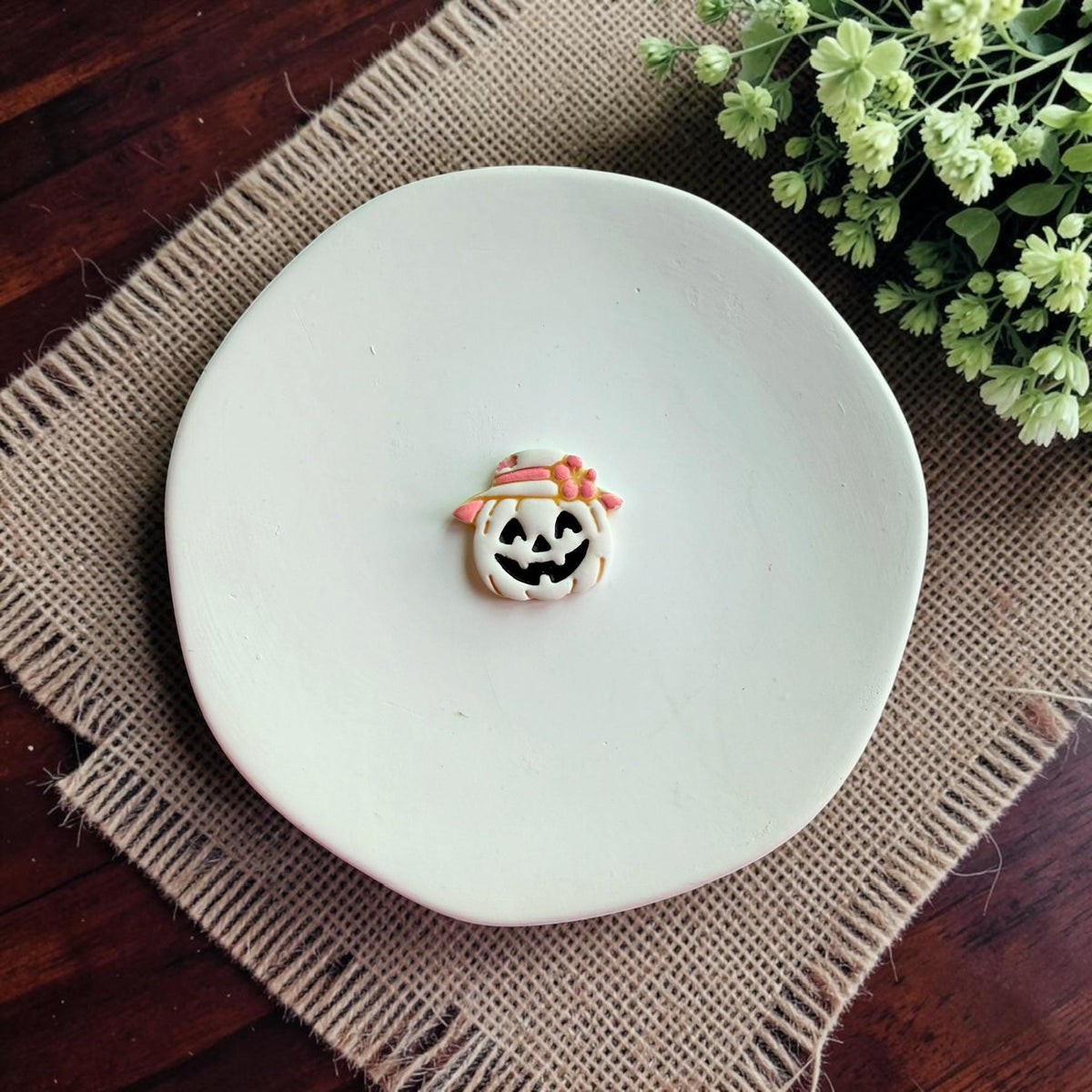 Finished polymer clay pumpkin earring featuring a smiling jack o lantern wearing a floral sun hat made with the harvest pumpkin cutter.