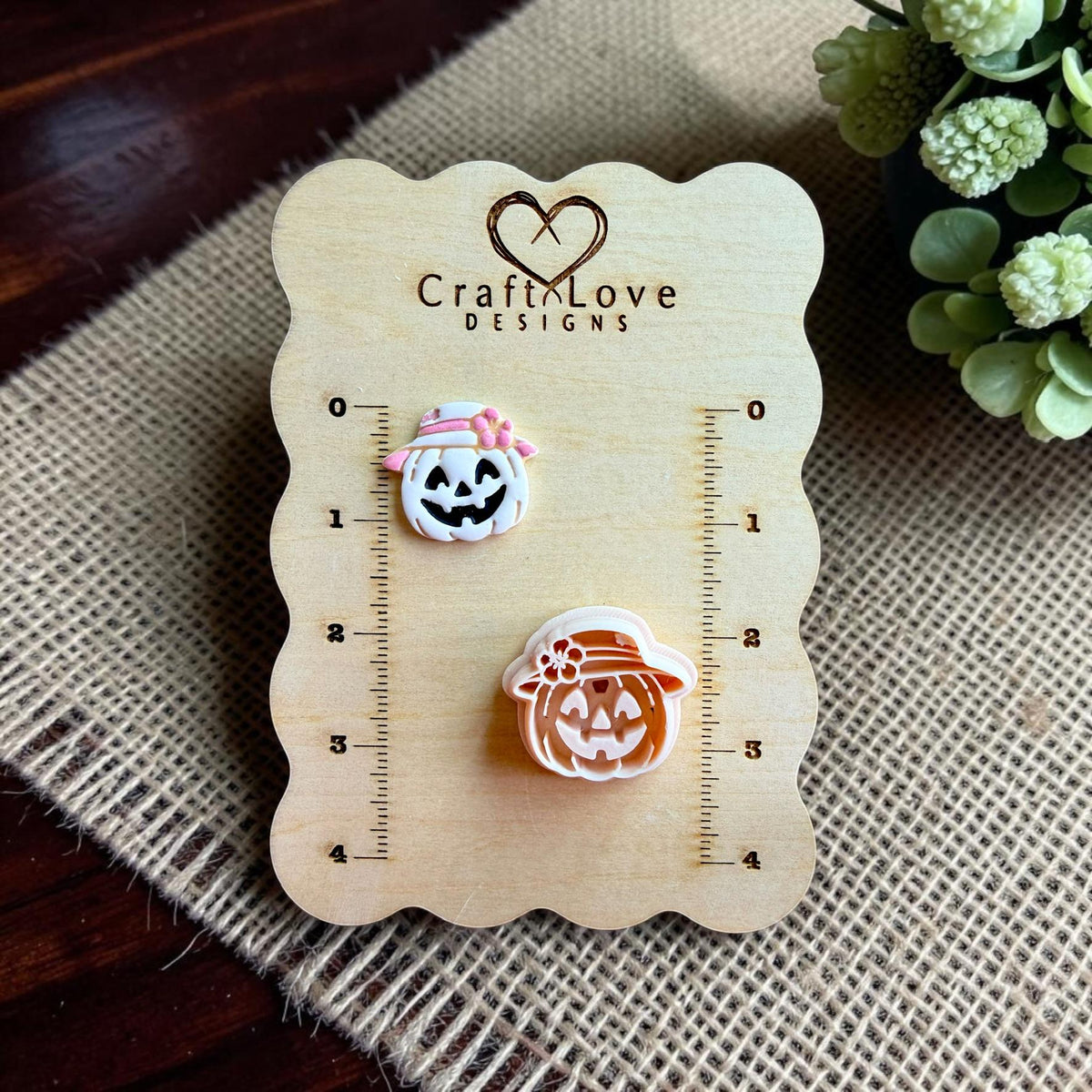 Harvest pumpkin polymer clay cutter with smiling jack o lantern wearing a sun hat displayed beside finished clay earring on wooden sizing board.