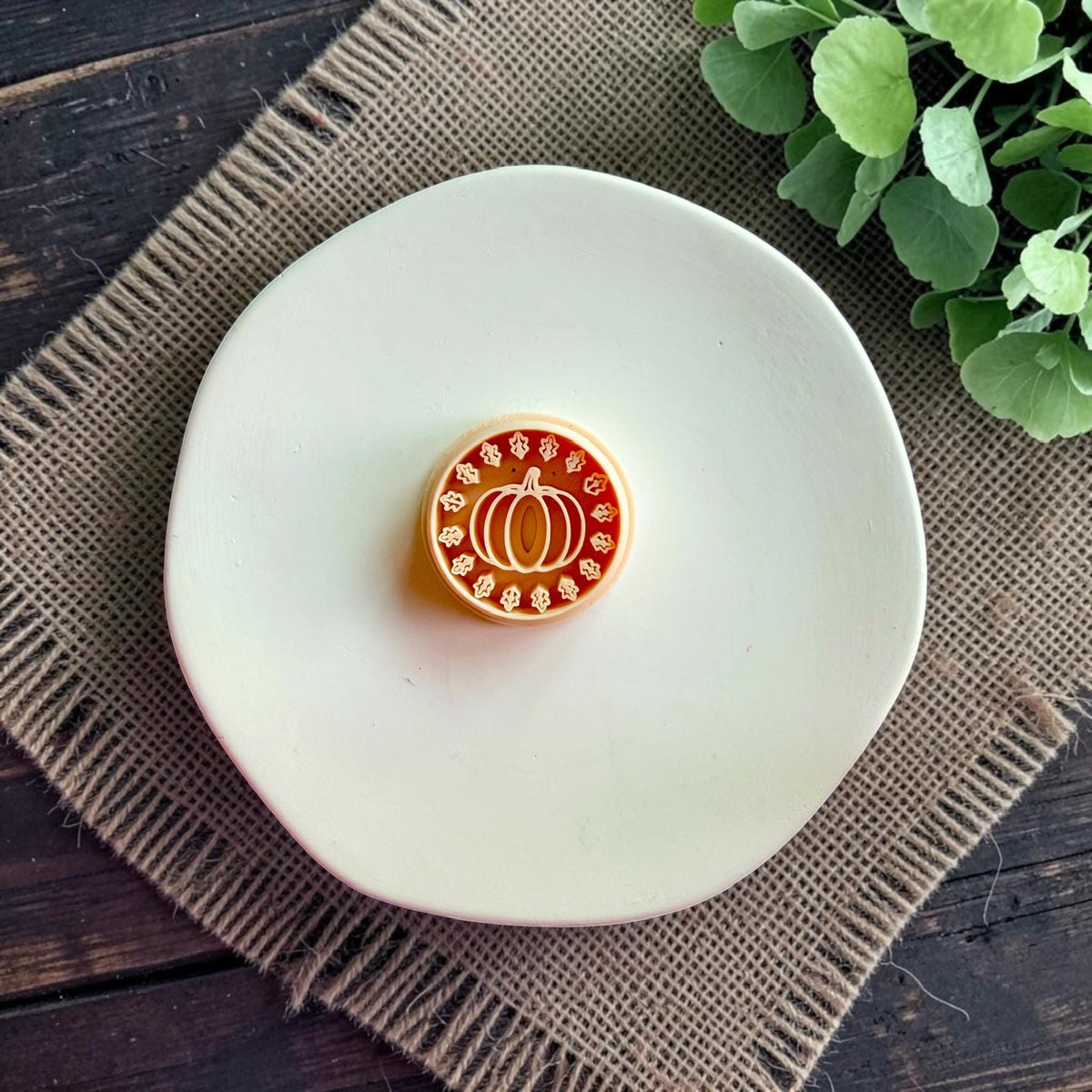 Pumpkin polymer clay cutter displayed alone on a white dish with autumn leaf wreath design visible.