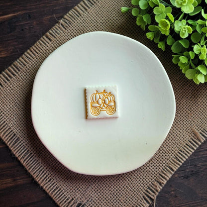 Finished white clay pumpkin wagon earring displayed on a white dish.