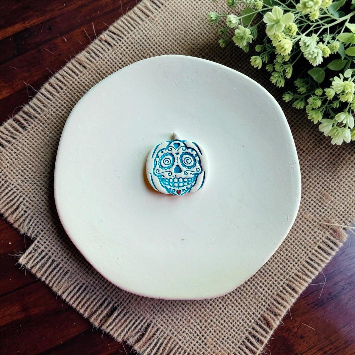 Finished white clay sugar skull pumpkin earring with blue details displayed on a white dish.