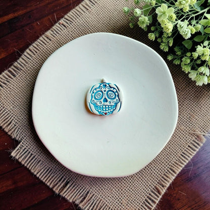 Finished white clay sugar skull pumpkin earring with blue details displayed on a white dish.