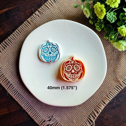 Finished sugar skull pumpkin earring beside the matching polymer clay cutter on a white dish with 40mm size shown.
