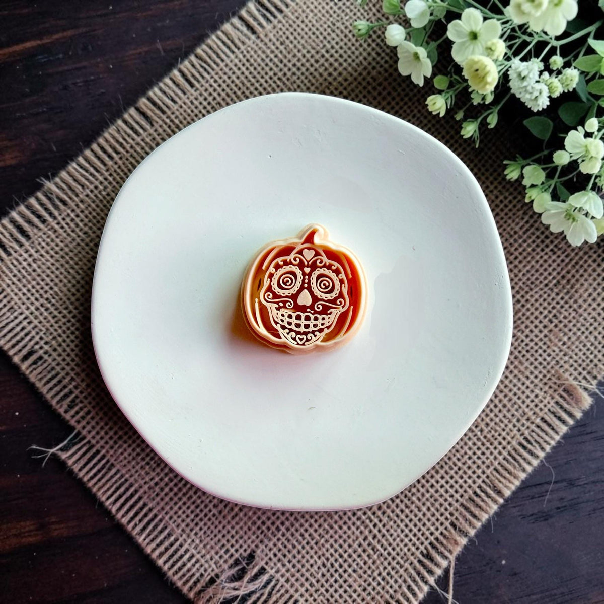 Sugar skull pumpkin polymer clay cutter displayed alone on a white dish.