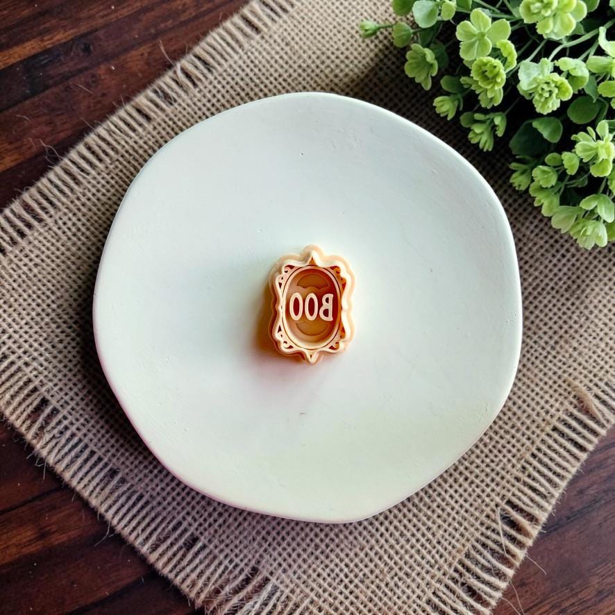 Finished white clay Boo design beside the matching polymer clay cutter displayed on a white dish.