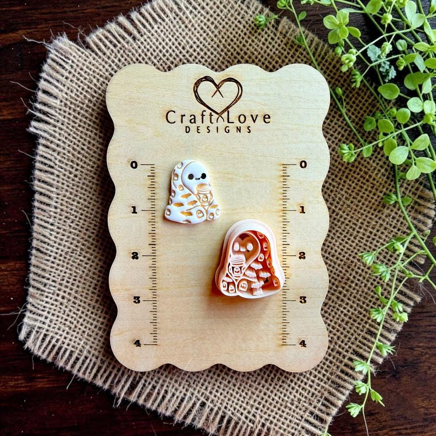 Finished cozy ghost holding a coffee cup beside the matching polymer clay cutter on a Craft Love Designs size board.