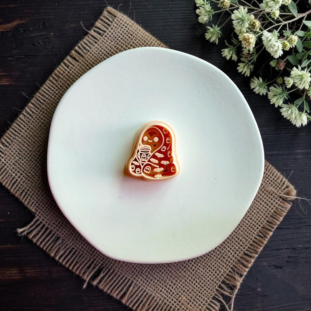 Cozy ghost polymer clay cutter featuring a ghost wrapped in a blanket holding a coffee cup displayed on a white dish.