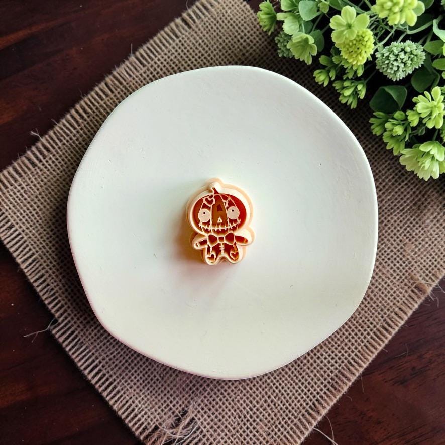 Stitched pumpkin doll polymer clay cutter displayed on a white dish.
