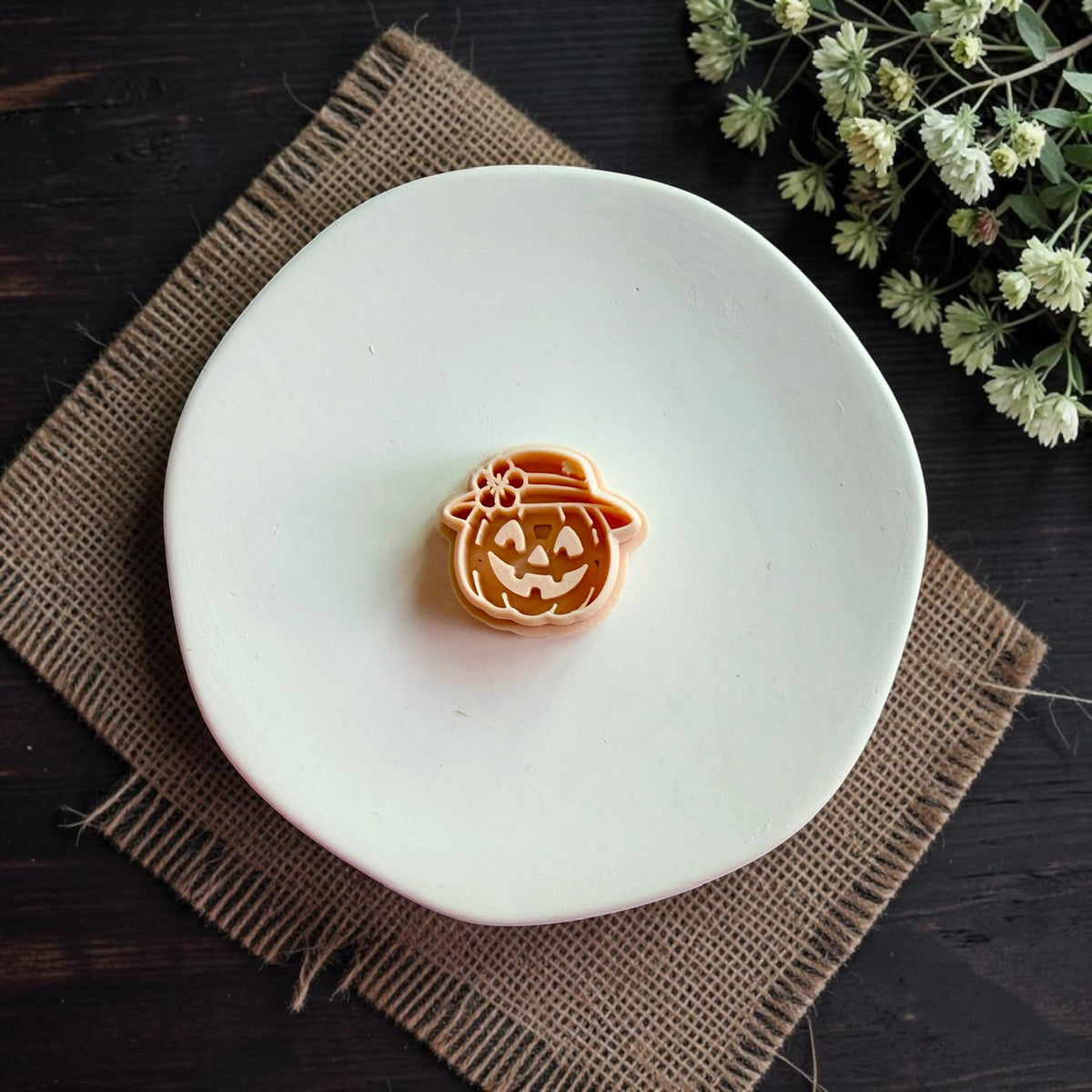 Harvest pumpkin polymer clay cutter featuring a smiling jack o lantern wearing a sun hat with flower detail for fall earring making.