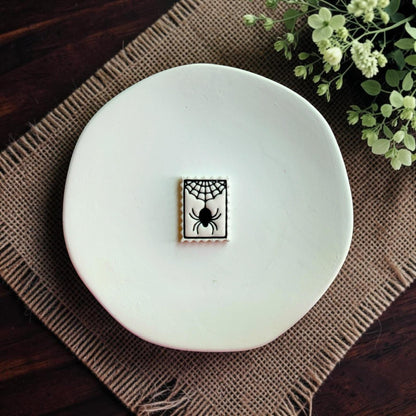 Finished white clay spider web design with black spider displayed on a white dish.